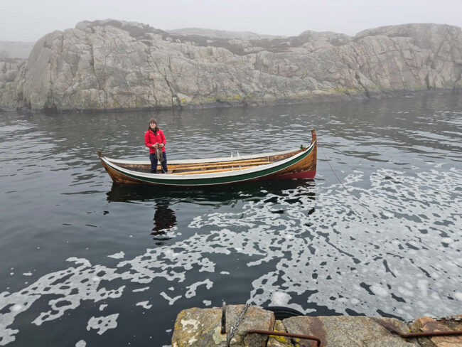 Ine-Lill står i rød jakke i Lofotr, like ved kai i Lindesnes